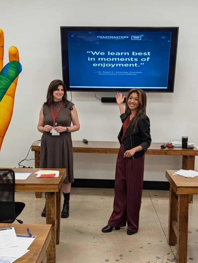 Two District 3 Toastmasters members at a Tucson leadership training, beside a screen showing founder Ralph Smedley's quote: We learn best in moments of enjoyment