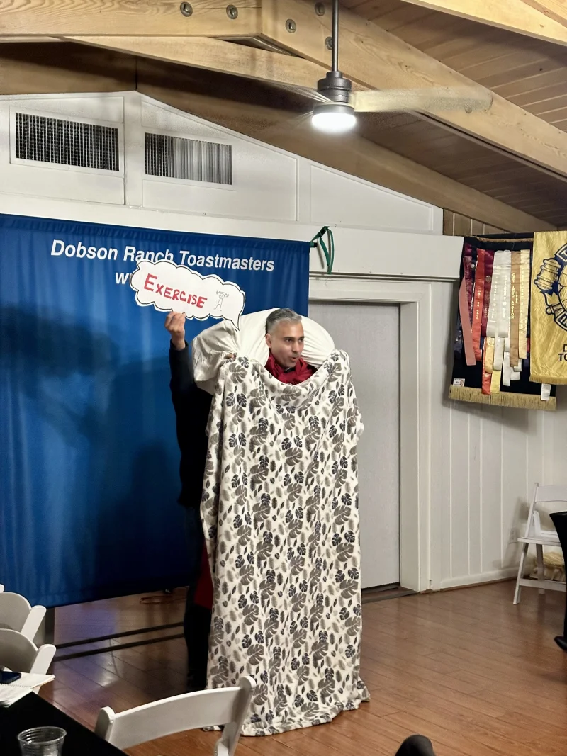 Rupesh Parbhoo delivering a speech at Dobson Ranch Toastmasters wrapped in a blanket as a prop