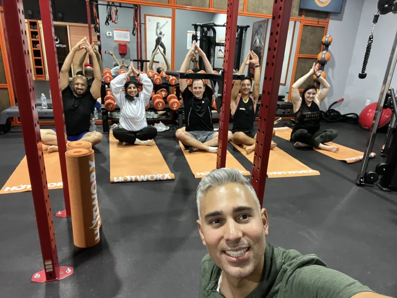 Rupesh Parbhoo teaching a yoga class with students in tree pose on orange mats